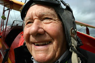 Old man in flying goggles with old plane in background